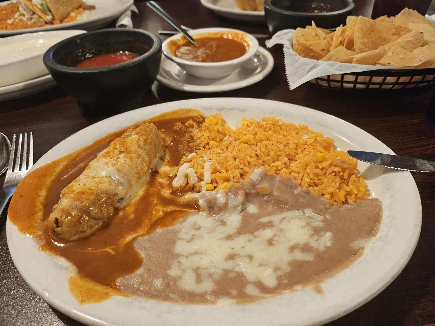 An enchilada under red sauce beside Mexican rice and refried beans on a white plate